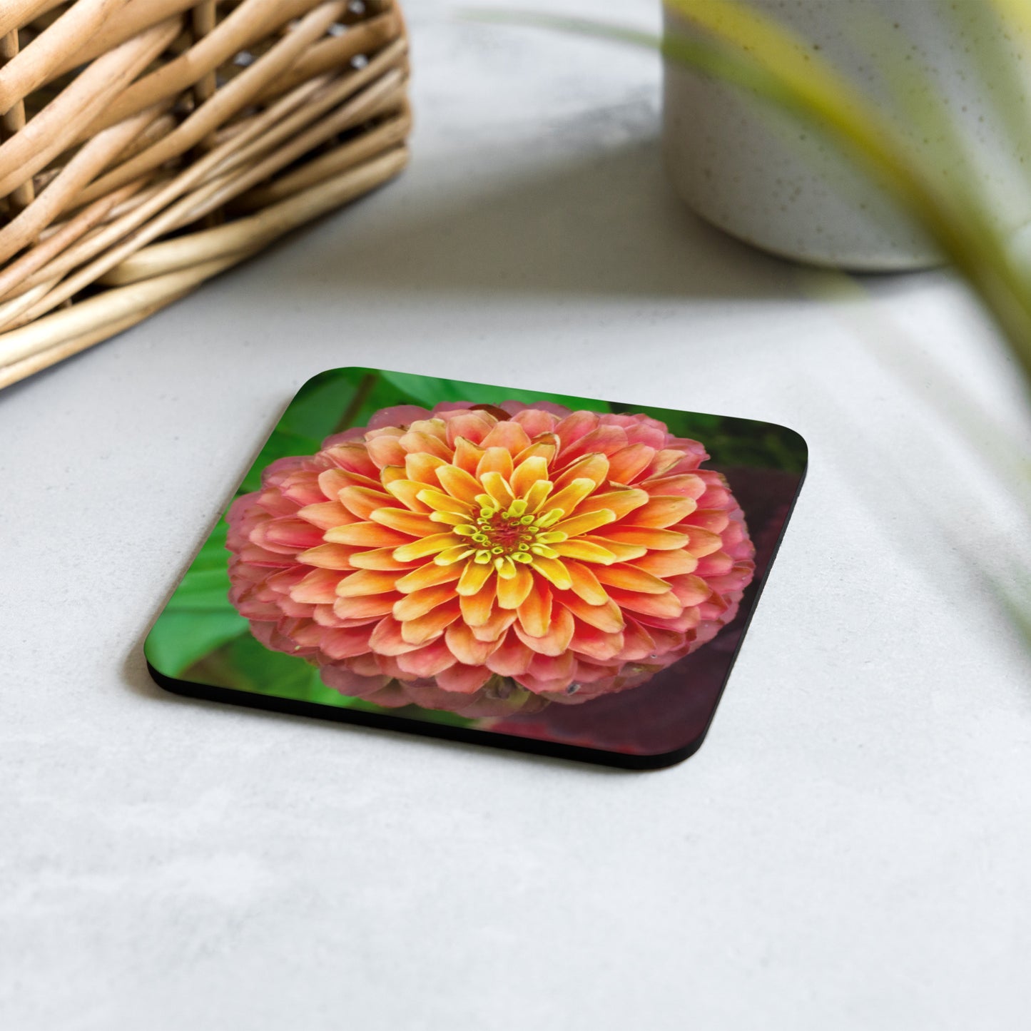 An artisan botanical coaster titled 'Layered Radiance' by Warlock Photography, featuring a macro photograph of a vibrant zinnia in sunset orange and pink tones.